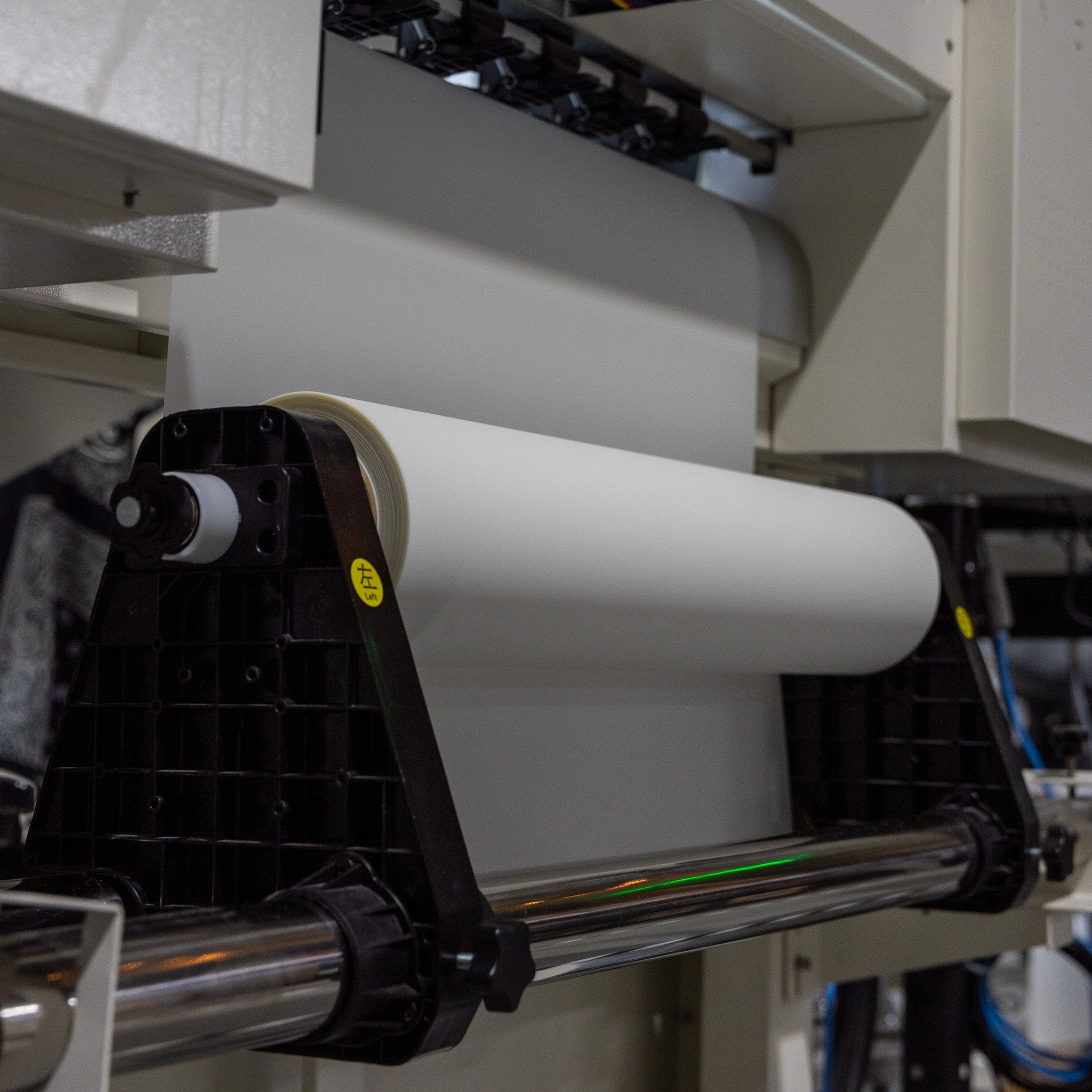 The 24in Hot Peel DTF Film - Double Side Matte by DTF Locker is mounted on a printing machine, ready for processing in an industrial facility with visible metal components and mechanical structures.